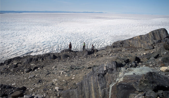 people standing on banded rocks in front of an ice field